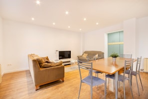 A modern living room with a sofa, TV, dining table, and chairs.