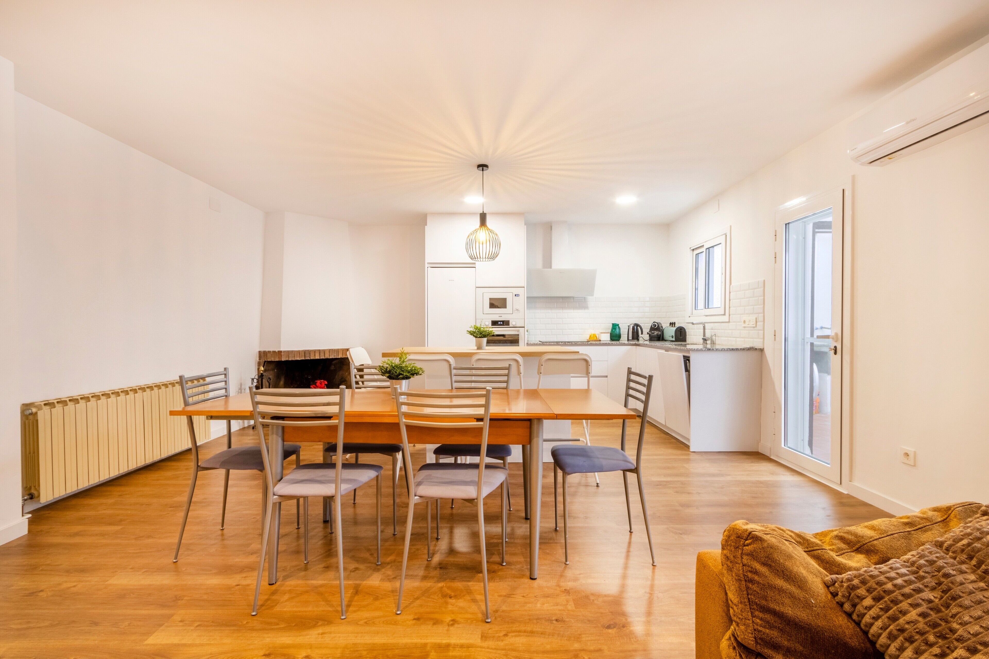 A modern kitchen with white cabinets, a dining table with chairs, and a pendant light.