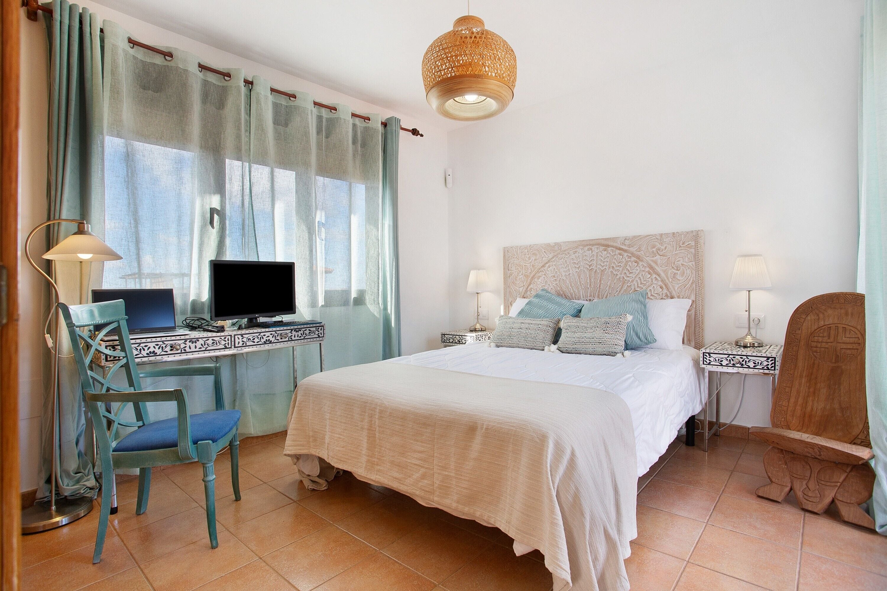 Et soveværelse med seng, skrivebord, stol, fjernsyn og dekorative lamper.