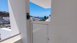 A balcony with a white door, a view of a coastal cityscape, and a small wall-mounted device.