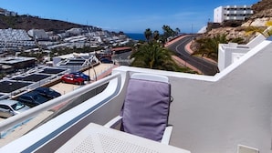 A balcony with a view of a coastal town, a parking area, and a road curving around the town.