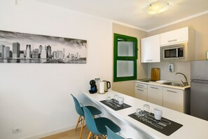 A compact kitchen with a cityscape mural, a green-framed door, and a dining area with teal chairs. - Vacation Apartment 'Dreams' with Sea View, Shared Pool and Wi-Fi (Puerto Rico)