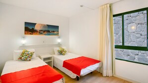 A room with two beds, a nightstand, a painting, a stone wall, and a window with curtains. - Vacation Apartment 'Dreams' with Sea View, Shared Pool and Wi-Fi (Puerto Rico)
