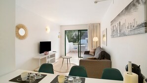 A modern living room with a dining area, a sofa, a TV, and a painting on the wall. - Vacation Apartment 'Dreams' with Sea View, Shared Pool and Wi-Fi (Puerto Rico)