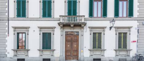 A building with a central wooden door, green shutters, and a small balcony.
