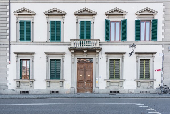 A building with a central wooden door, green shutters, and a small balcony.