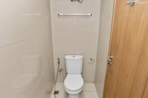 A small, clean bathroom with a toilet, a handrail, and a wooden door. - OYO 93432 Tree Room Hotel (Tangerang)
