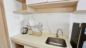 A kitchen with a stainless steel sink, a dish rack, and a kettle. - OYO 93432 Tree Room Hotel (Tangerang)