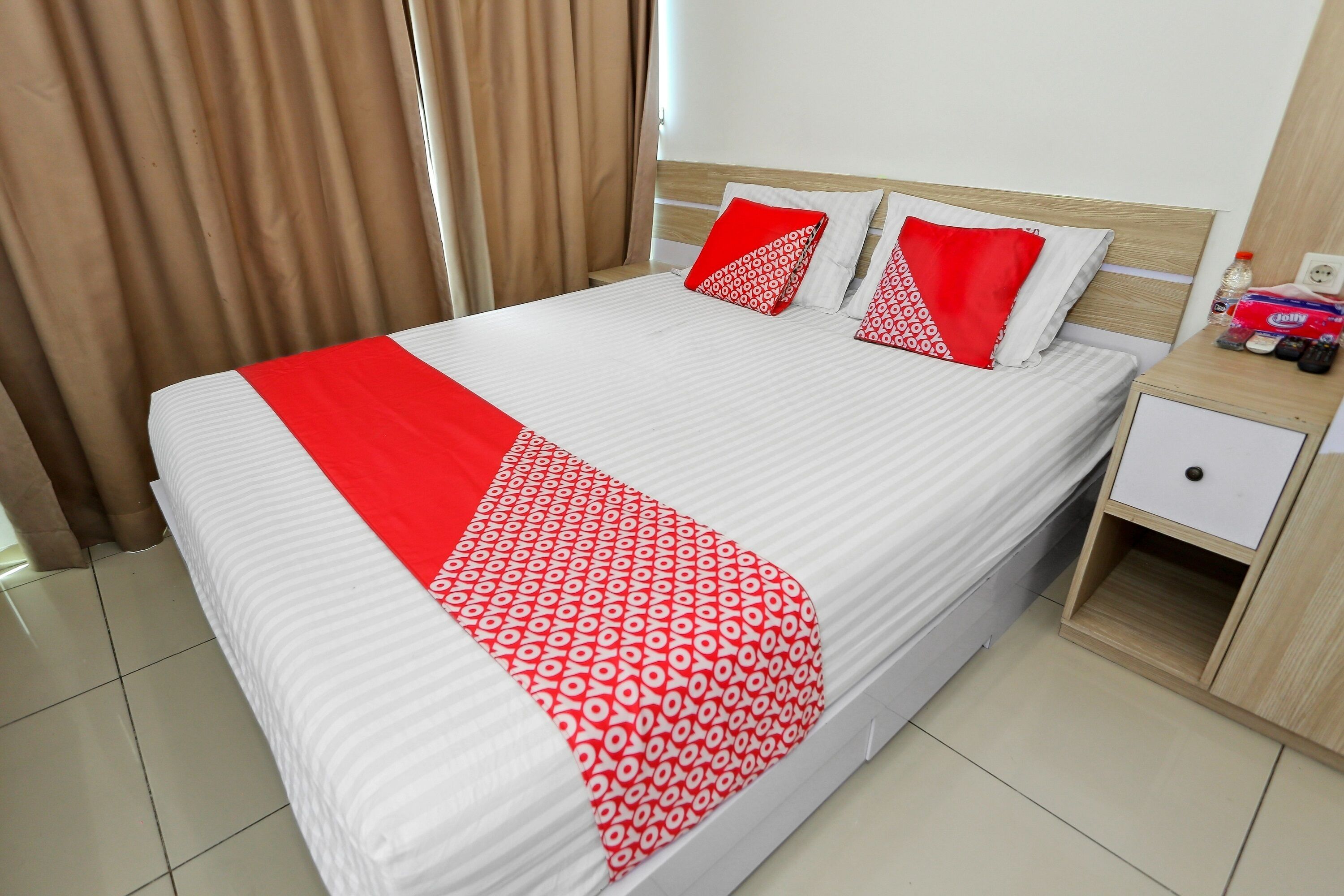 A neatly made bed with a white and red bedspread, two red pillows, and a wooden headboard.