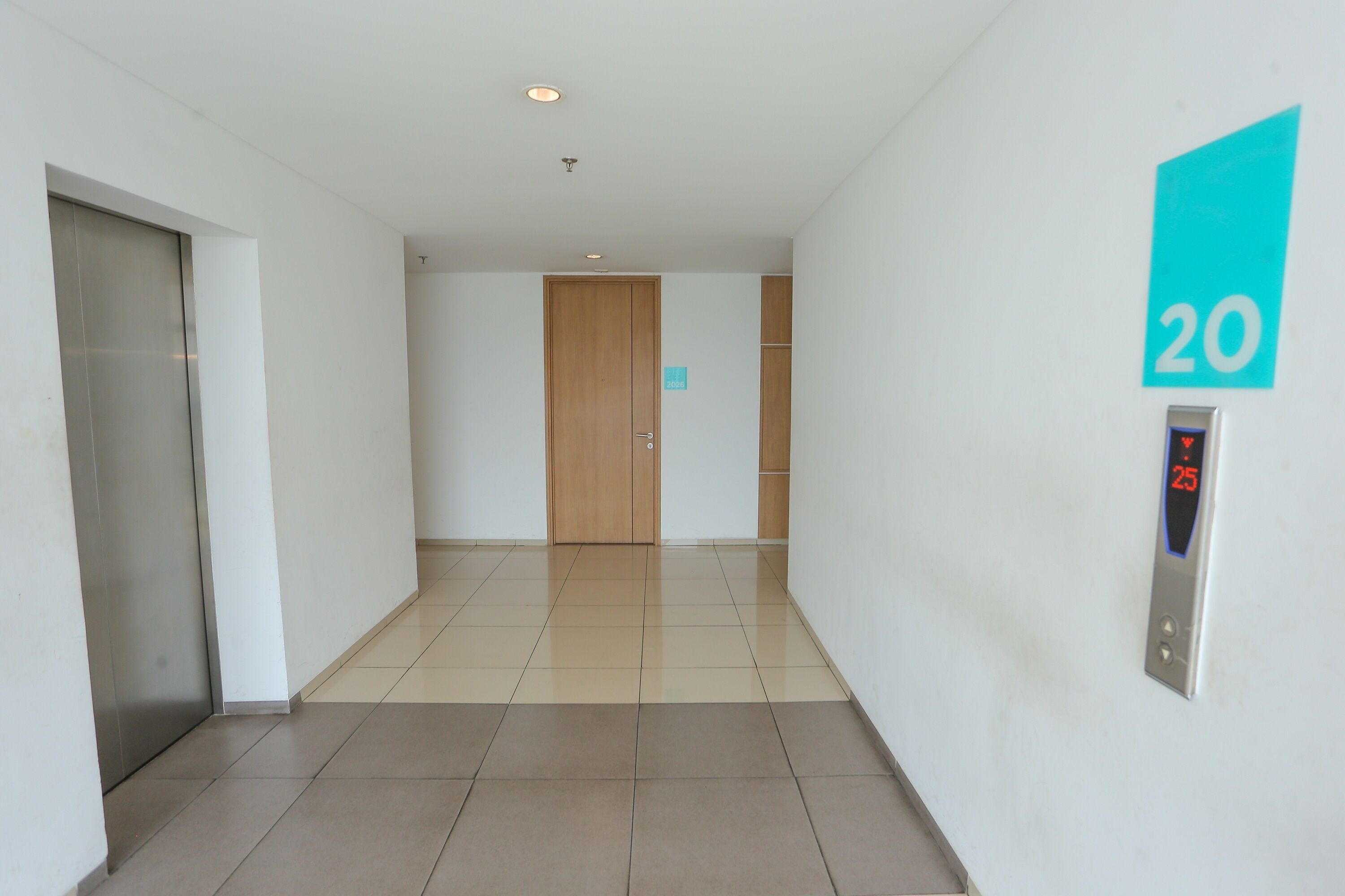 A hallway with a wooden door, a digital elevator control panel, and a wall-mounted sign indicating room number 20.