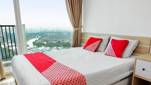 A modern hotel room with a large bed, a nightstand, and a view of a cityscape through large windows. - OYO 93432 Tree Room Hotel (Tangerang)