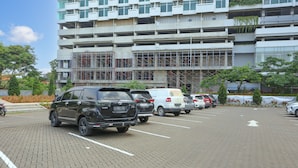 A parking lot with multiple cars and a multi-story building with scaffolding in the background. - OYO 93432 Tree Room Hotel (Tangerang)