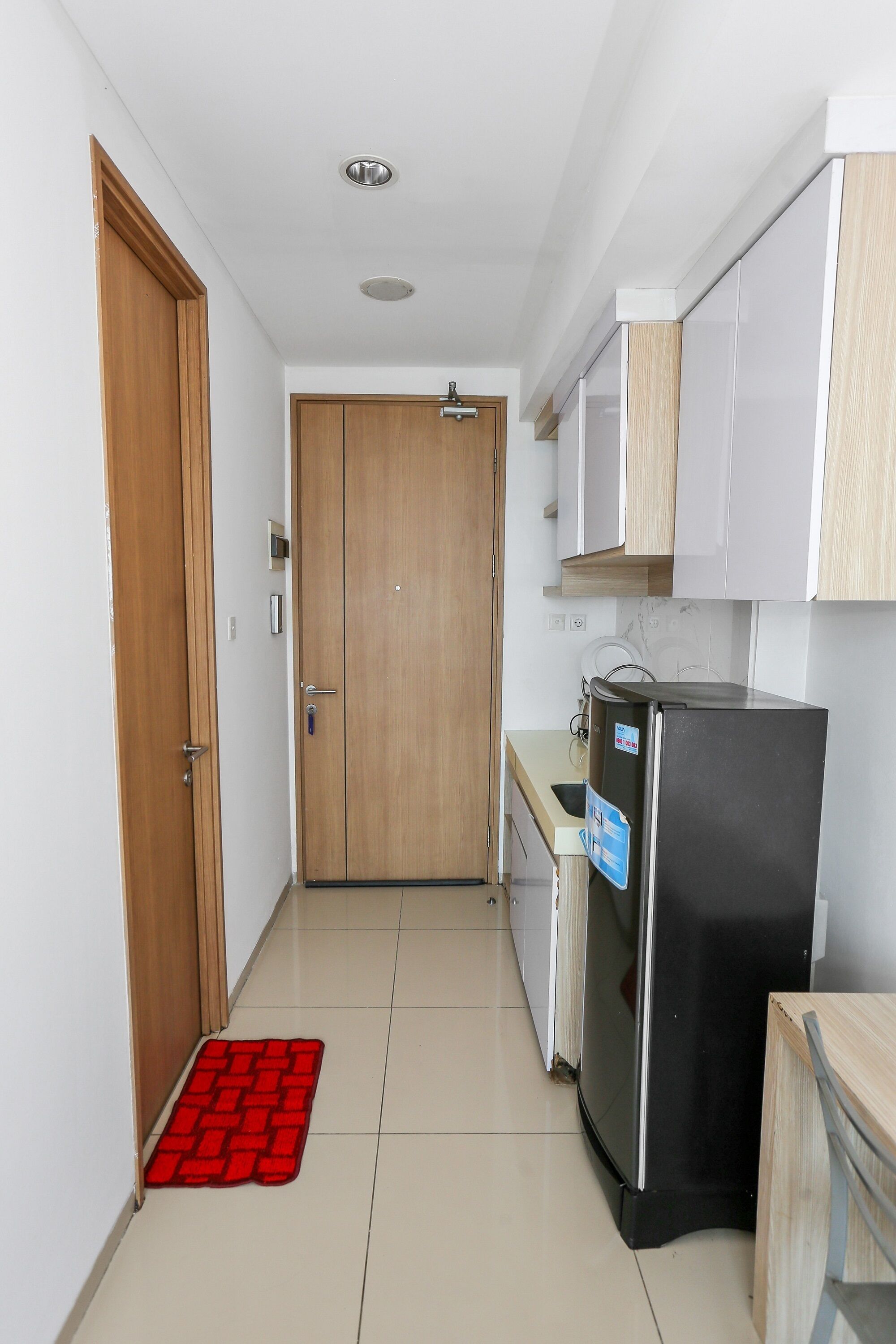 A narrow hallway with a wooden door, a refrigerator, and a microwave.