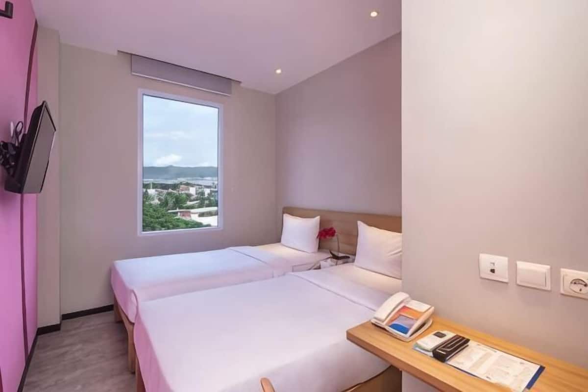 Une chambre dâhĂŽtel avec deux lits, un bureau avec un tĂ©lĂ©phone et des documents, une fenĂȘtre donnant sur un paysage agrĂ©able et un tĂ©lĂ©viseur fixĂ© au mur.