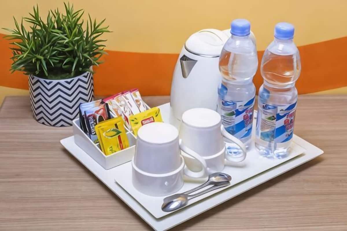 A tray with a white mug, a white cup, two water bottles, a spoon, and some food packets on a table.