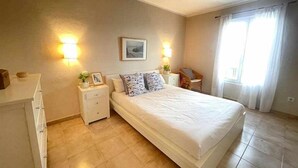 Un dormitorio con una cama, mesitas de noche, una silla y una ventana con cortinas.