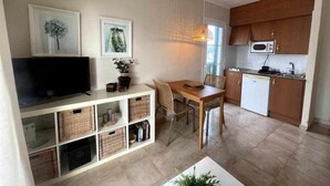 Un espacio habitable compacto con comedor, kitchenette y televisor en un estante.