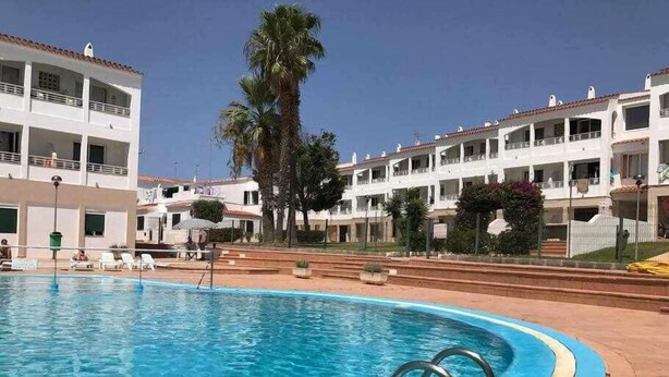 Una piscina con agua azul cristalina, rodeada por una solana con baldosas. Se observan sillas de descanso y una palmera al fondo.