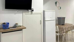 A compact kitchen with a white refrigerator, a microwave, and a small table with a patterned tablecloth. - Macarelleta- Apartamento con Piscina (Cala Blanes)