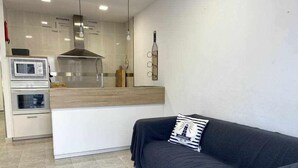 A modern kitchen with a built-in oven, microwave, and a stainless steel range hood. There is a wooden countertop and a black sofa with a striped pillow. - Macarelleta- Apartamento con Piscina (Cala Blanes)