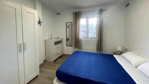 A bedroom with a bed, a wardrobe, a dresser, a mirror, and a window with curtains. - Macarelleta- Apartamento con Piscina (Cala Blanes)