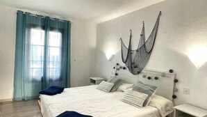 Une chambre à coucher comprenant un lit, deux tables de chevet, un luminaire fixé au mur et une fenêtre avec des rideaux.