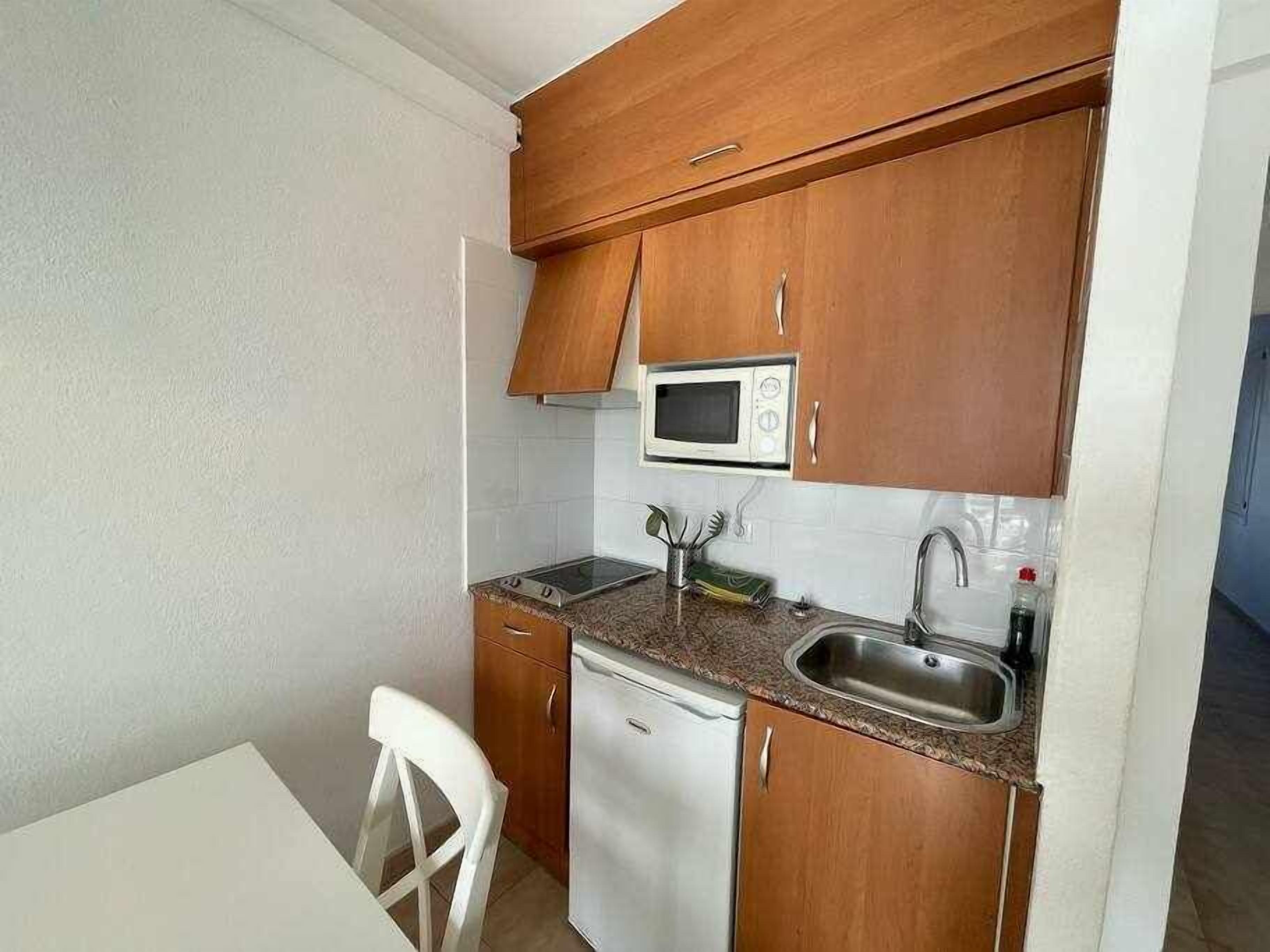 A compact kitchen with wooden cabinets, a microwave, a sink, and a dishwasher.