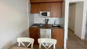 A compact kitchen with wooden cabinets, a microwave, a sink, and two white chairs.