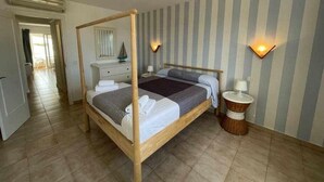 A four-poster bed with a wooden frame, a bedside table with a lamp, and a striped wall.