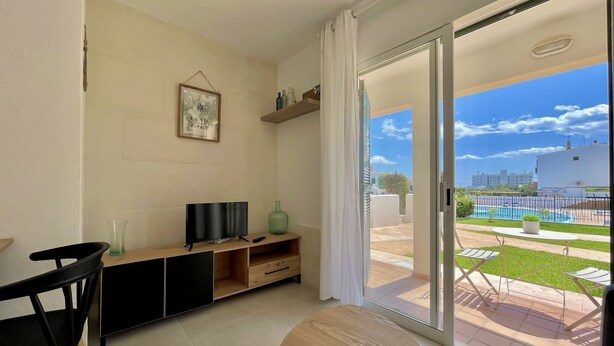 A modern living room with a TV, a small table, and a sliding glass door leading to an outdoor patio with a pool.