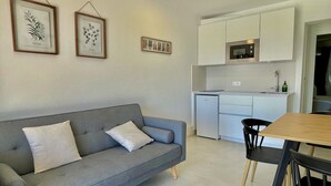 A compact living space with a grey sofa, a small dining table, and a kitchenette area.