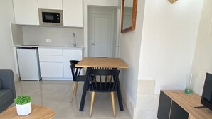 A modern living room with a wooden dining table and chairs, a small coffee table with a plant, and a TV on a wooden stand.