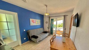 Un espacio habitable compacto con kitchenette, un sofá, una mesa de comedor y un televisor montado en la pared.