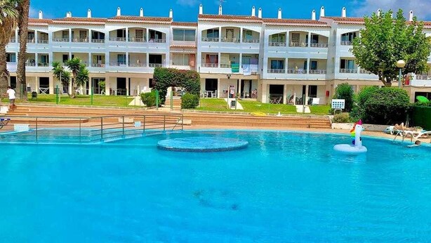 Un hotel con piscina, varios balcones y un césped bien cuidado.