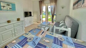Una habitación con una mesa de comedor, un sofá, un televisor y vistas al exterior.
