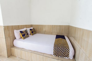 A single bed with a white mattress, two pillows with geometric patterns, and a blue and yellow polka dot blanket. - Hotel O Penginapan Mekar Sari Near PT. Lombok Menara Energygas (Kuripan)