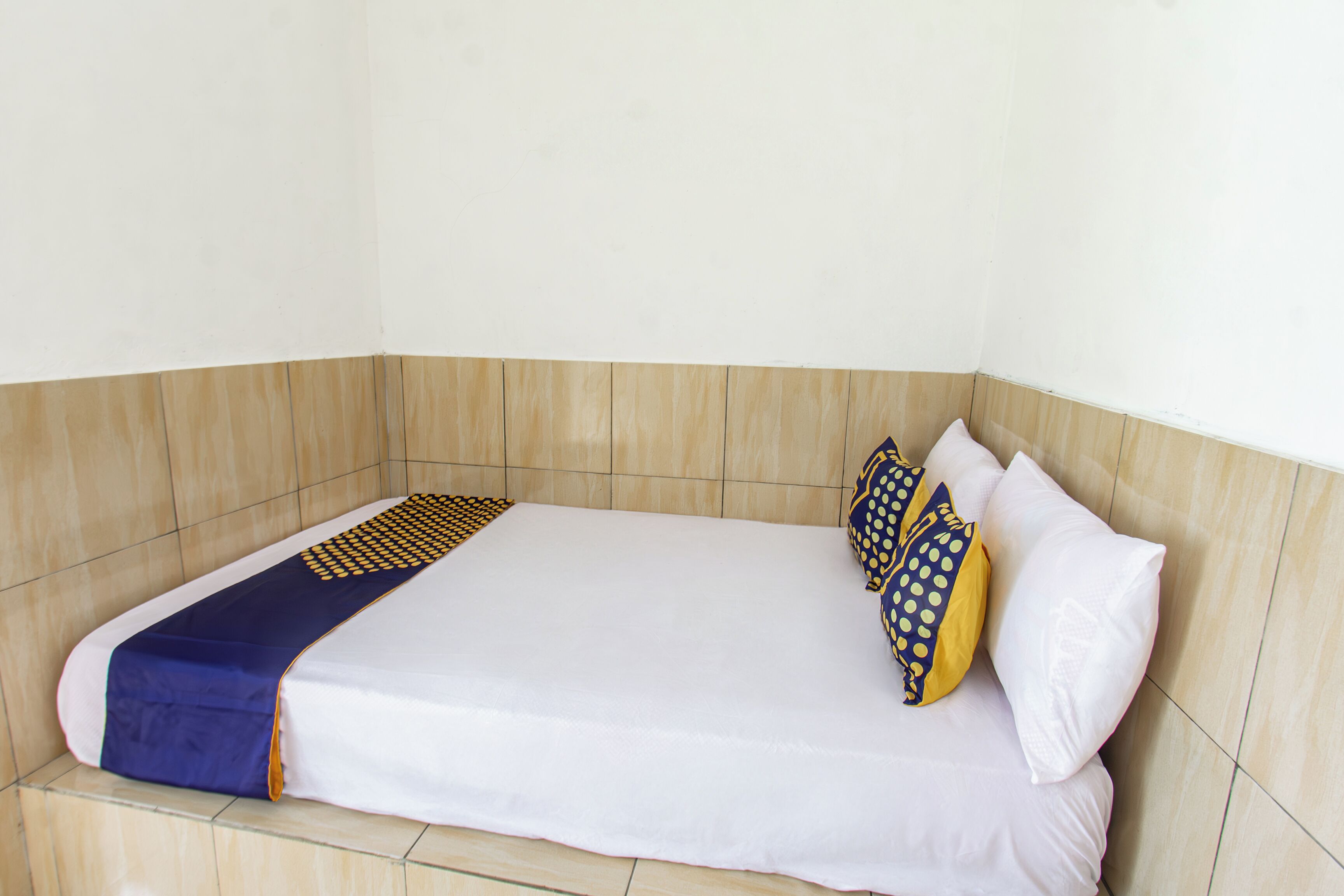 Uma cama de solteiro com colchão branco, colcha azul e amarela estampada e dois travesseiros com padrões semelhantes.