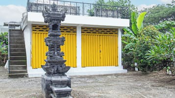A building with a staircase leading to a balcony, a large yellow door, and a stone structure in front.