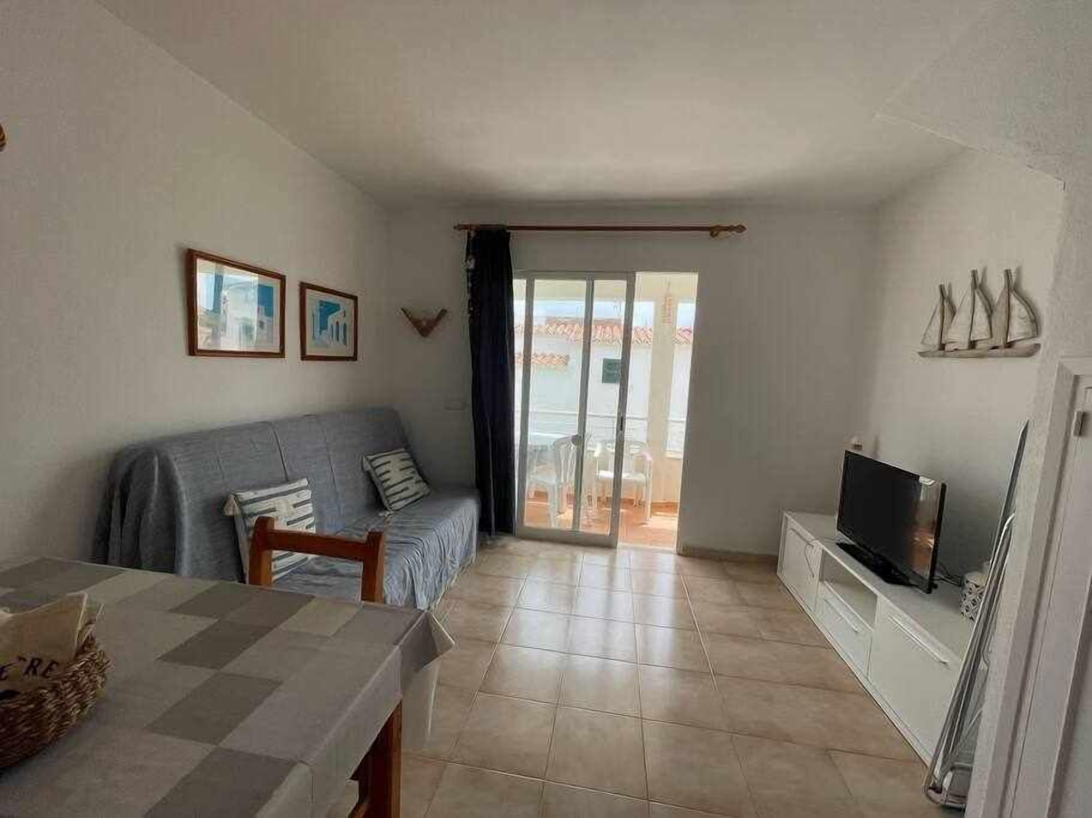 A living room with a sofa, a TV, and a balcony with a view.