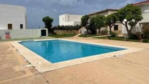 Una piscina rectangular con superficie de agua azul cristalina, rodeada por una zona pavimentada y un muro bajo.