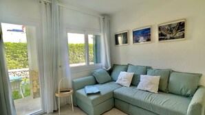 Una sala de estar con un sofá seccional verde, una mesita auxiliar y un ventanal corredizo que da a un espacio exterior. Hay dos cuadros en la pared.