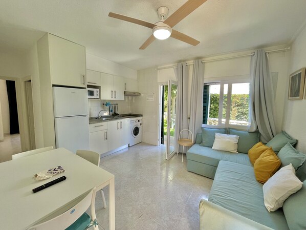A compact living space with a kitchenette, a dining area, and a sofa with cushions.