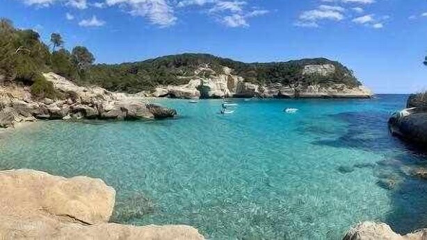 Un paisaje costero con aguas turquesas cristalinas, formaciones rocosas y un barco a lo lejos.