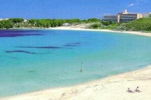 Una playa con agua turquesa cristalina, una orilla de arena y un edificio al fondo.