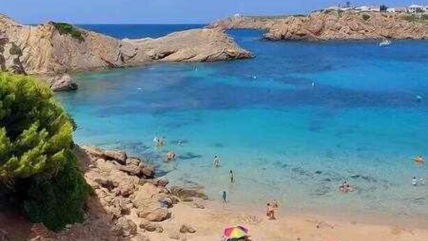 A beach with clear blue water, rocky terrain, and a few people swimming.