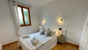 A bedroom with a bed, pillows, a nightstand with a lamp, and a window with curtains.