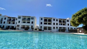 A clear pool with a view of a white building with balconies and a tree to the right.