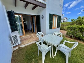 Un patio exterior con una mesa, sillas, una puerta corrediza de vidrio y un equipo de aire acondicionado.