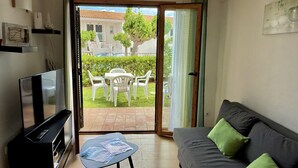 Un salon équipé d’un téléviseur, d’un canapé, d’une petite table et d’une porte-fenêtre coulissante donnant sur une terrasse extérieure avec une table et des chaises.