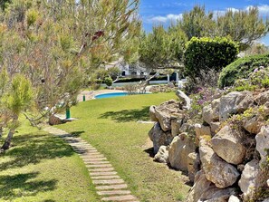 Un jardín ajardinado con un sendero de piedra, una piscina y vistas a una casa.
